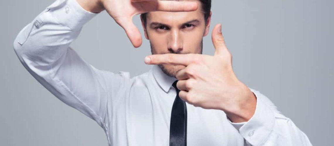 Businessman making frame gesture over gray background and looking at camera
